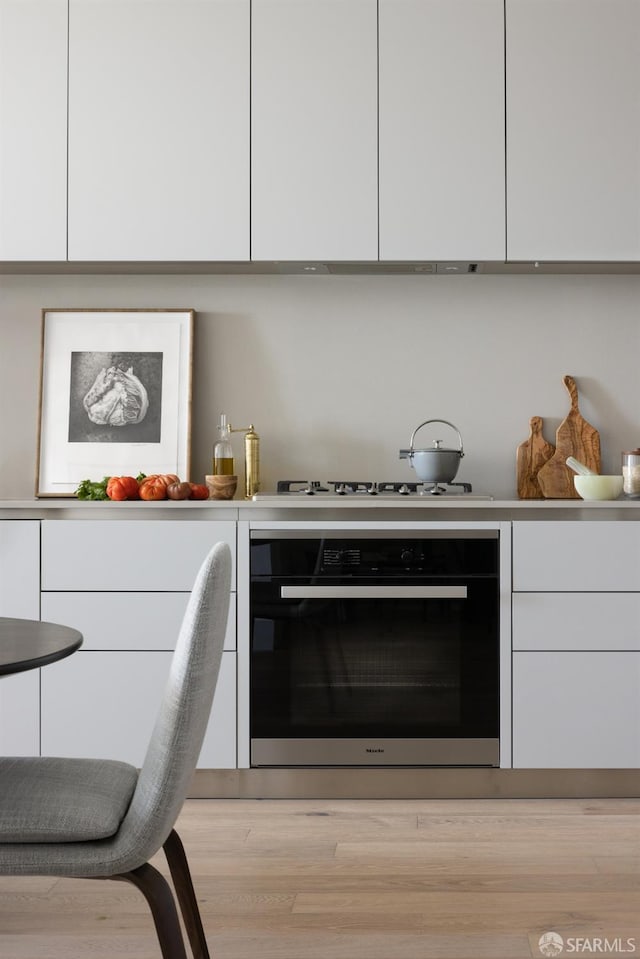 kitchen with white cooktop, modern cabinets, white cabinetry, and black oven