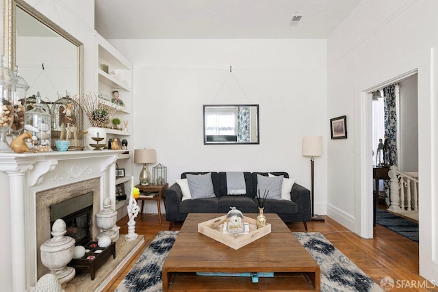 living room featuring built in shelves, a high end fireplace, plenty of natural light, and wood finished floors