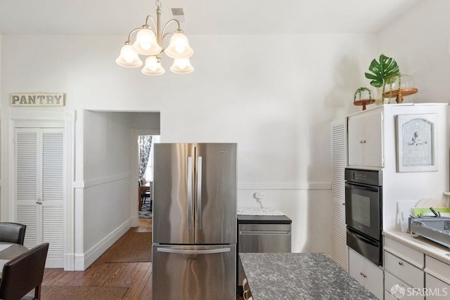 kitchen with a notable chandelier, wood finished floors, black oven, freestanding refrigerator, and a warming drawer