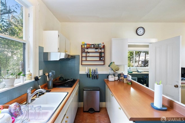 kitchen with tile patterned flooring, black cooktop, a sink, white cabinets, and tasteful backsplash