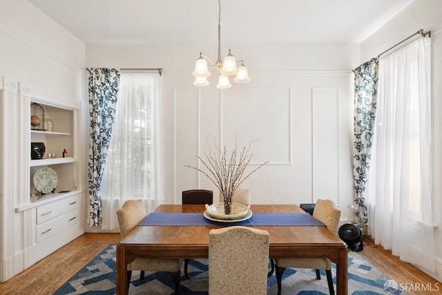 dining area with built in shelves, light wood finished floors, and an inviting chandelier