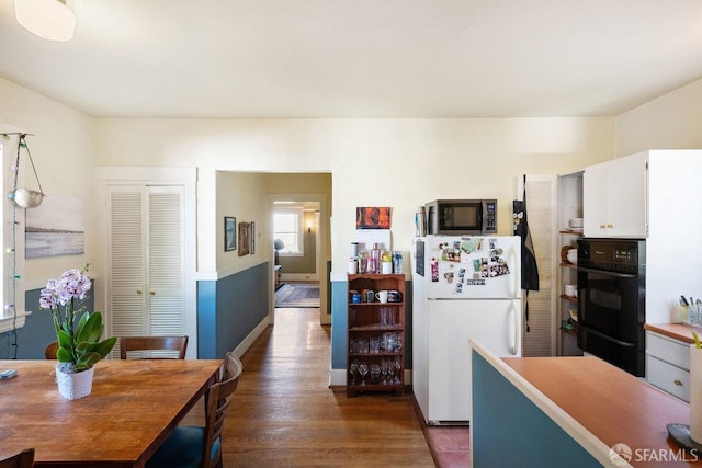 kitchen featuring stainless steel microwave, dobule oven black, dark wood-type flooring, freestanding refrigerator, and white cabinets