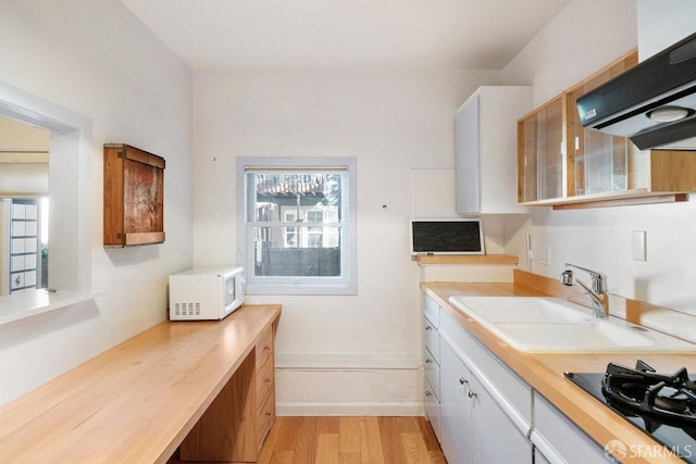 kitchen with range hood, white microwave, light wood-style floors, a sink, and black gas stovetop