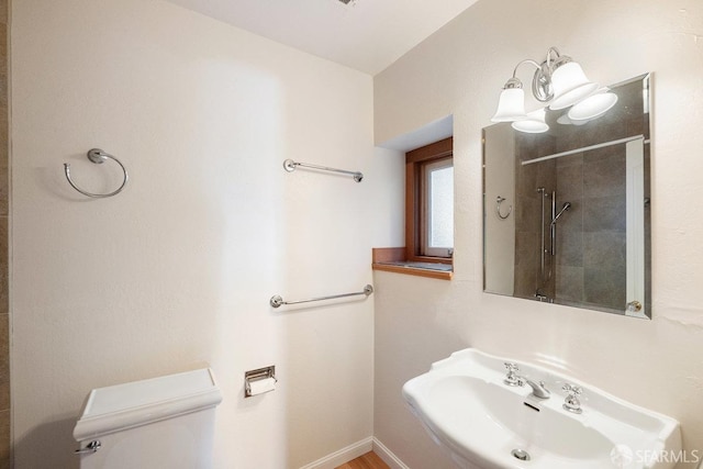 bathroom with baseboards, a sink, a tile shower, and toilet