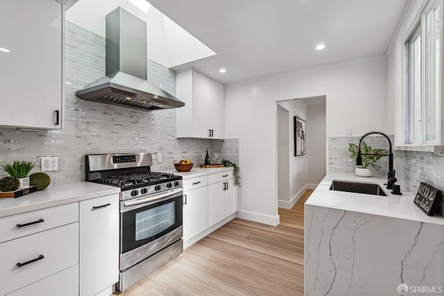 kitchen featuring wall chimney range hood, sink, white cabinetry, light stone countertops, and gas range