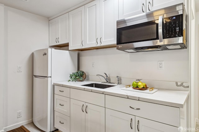 kitchen featuring light stone countertops, white fridge, sink, and white cabinets