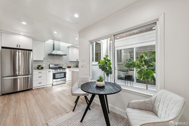 kitchen featuring backsplash, stainless steel appliances, light hardwood / wood-style floors, white cabinets, and wall chimney exhaust hood