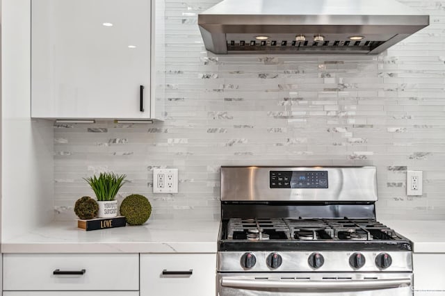 kitchen with stainless steel gas stove, white cabinetry, light stone countertops, and wall chimney exhaust hood