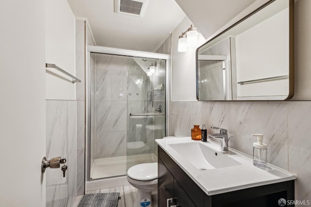 bathroom featuring vanity, toilet, a shower with door, and tile walls