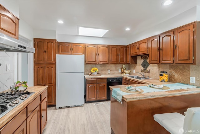 kitchen with a skylight, sink, white refrigerator, kitchen peninsula, and light hardwood / wood-style floors