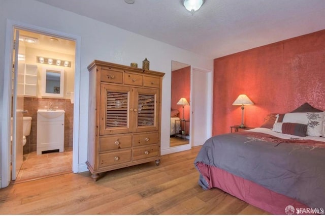 bedroom featuring ensuite bath, light hardwood / wood-style flooring, and tile walls