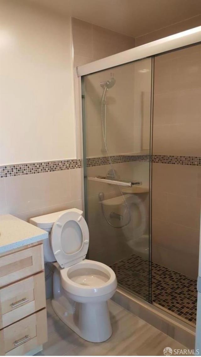 bathroom with walk in shower, vanity, toilet, and tile walls