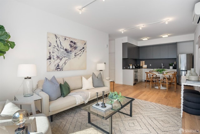 living room featuring a wall unit AC, track lighting, light hardwood / wood-style flooring, and sink