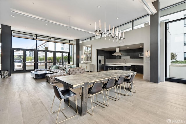 dining room with french doors, expansive windows, sink, light hardwood / wood-style flooring, and a towering ceiling