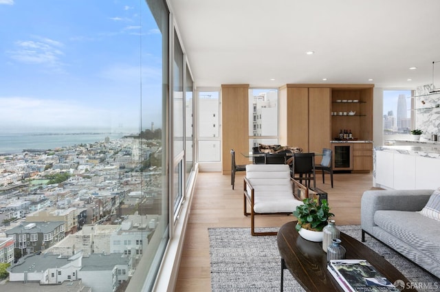 living room with a wall of windows, light hardwood / wood-style floors, beverage cooler, and a water view