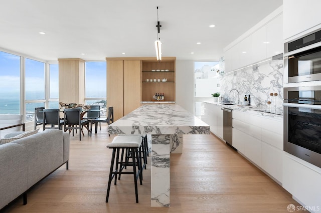 kitchen featuring light wood-type flooring, white cabinetry, hanging light fixtures, a water view, and appliances with stainless steel finishes