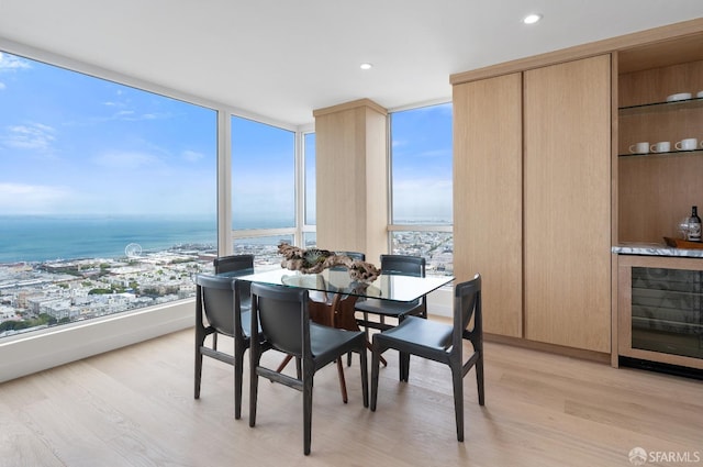 dining room featuring expansive windows, wine cooler, light hardwood / wood-style floors, and a water view