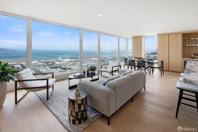 living room with a water view, light hardwood / wood-style floors, and a wall of windows