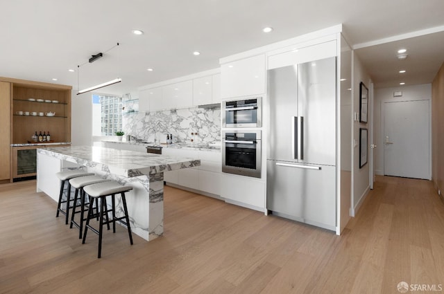 kitchen with light hardwood / wood-style floors, a center island, white cabinetry, a kitchen breakfast bar, and appliances with stainless steel finishes