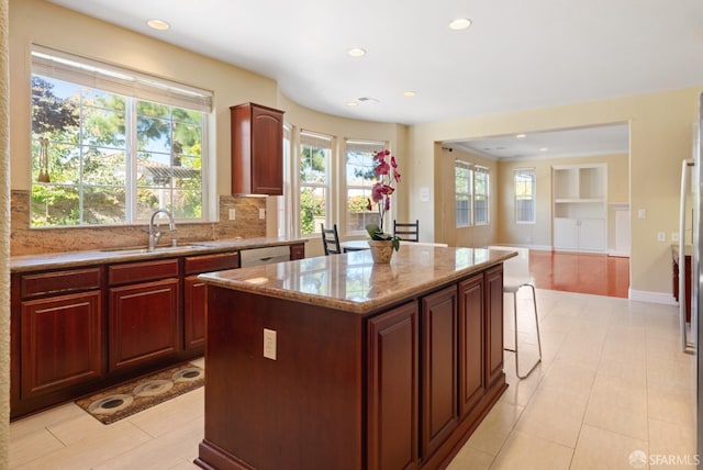 kitchen with light stone countertops, a center island, sink, built in features, and a kitchen bar