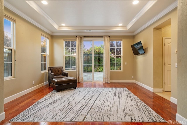 living area featuring a tray ceiling, crown molding, a healthy amount of sunlight, and light hardwood / wood-style floors