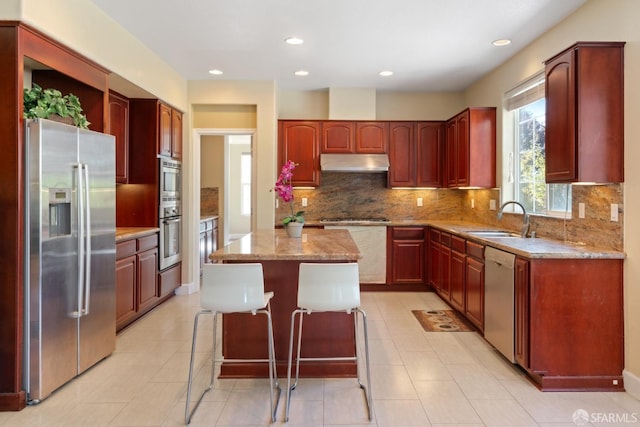 kitchen featuring decorative backsplash, appliances with stainless steel finishes, a breakfast bar, sink, and a center island