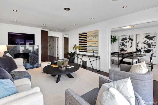 living area featuring a premium fireplace, recessed lighting, wood finished floors, and crown molding