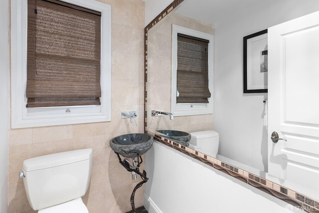 half bath featuring a sink, toilet, and tile walls