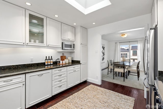 kitchen with appliances with stainless steel finishes, white cabinets, glass insert cabinets, and dark wood-type flooring