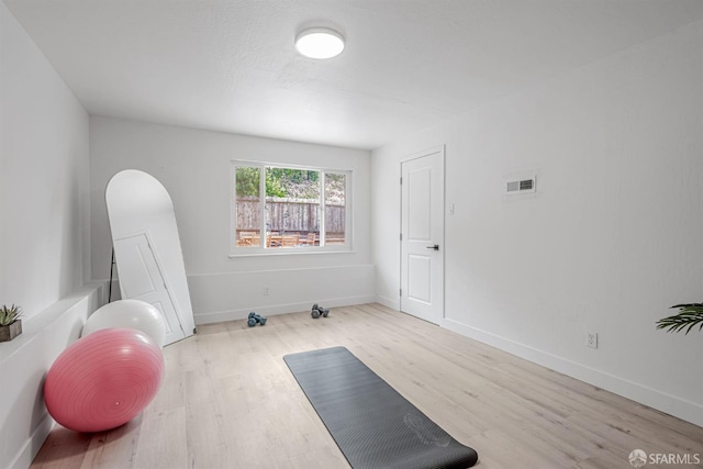 workout area featuring baseboards, arched walkways, visible vents, and wood finished floors