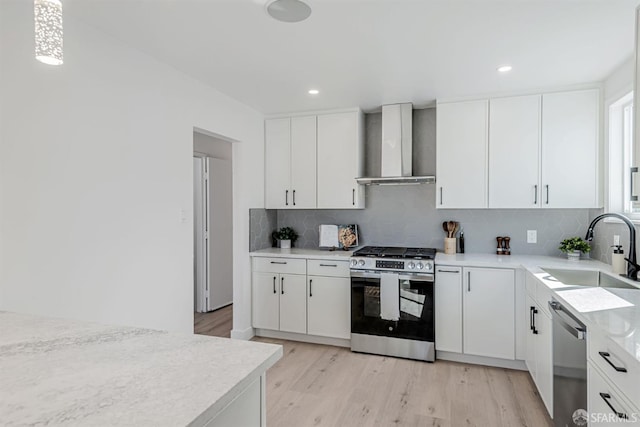 kitchen featuring light wood finished floors, a sink, light countertops, appliances with stainless steel finishes, and wall chimney exhaust hood