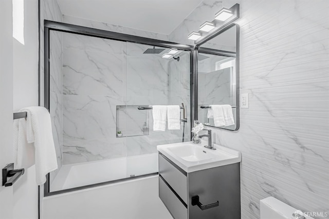 bathroom with toilet, vanity, tile walls, and bath / shower combo with glass door