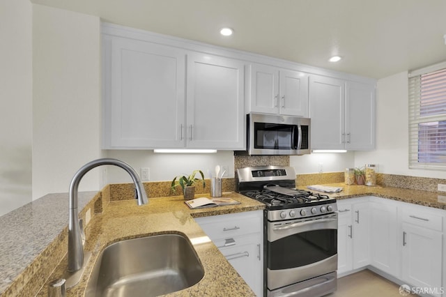 kitchen featuring a sink, stainless steel appliances, light stone counters, and white cabinetry