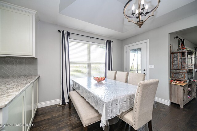 dining room with baseboards, a notable chandelier, a tray ceiling, and dark wood-type flooring