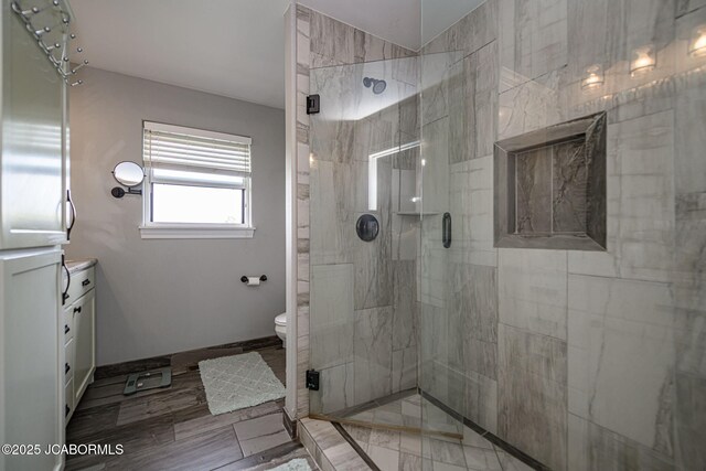 bathroom with baseboards, vanity, a shower stall, and toilet