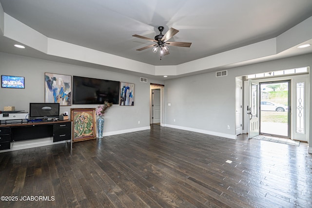 living room featuring a ceiling fan, a tray ceiling, visible vents, baseboards, and dark wood-style floors