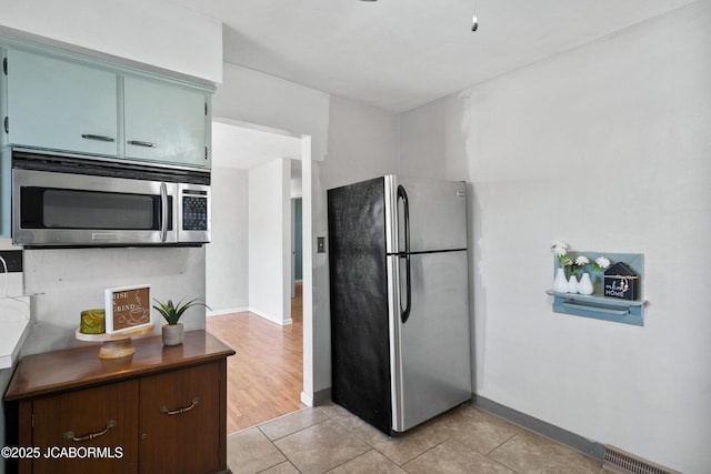 kitchen featuring blue cabinets, visible vents, stainless steel appliances, light tile patterned floors, and baseboards