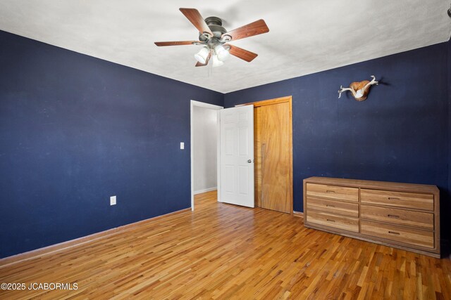 unfurnished bedroom featuring baseboards, wood finished floors, a closet, and ceiling fan