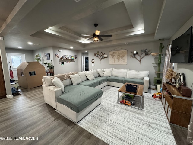 living room with hardwood / wood-style flooring, ceiling fan, and a raised ceiling