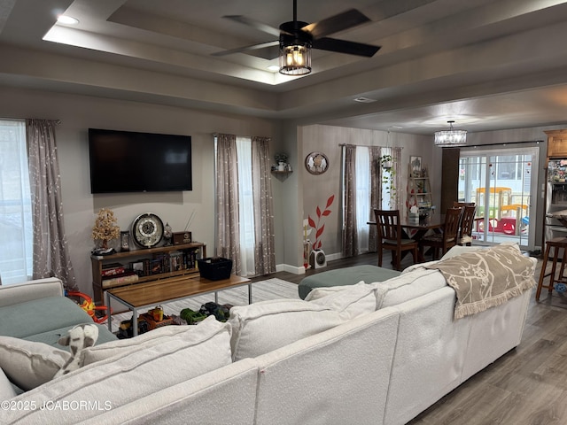 living room featuring wood-type flooring, ceiling fan with notable chandelier, and a tray ceiling