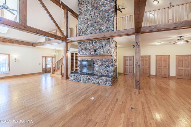 unfurnished living room with a stone fireplace, light hardwood / wood-style flooring, high vaulted ceiling, and ceiling fan with notable chandelier