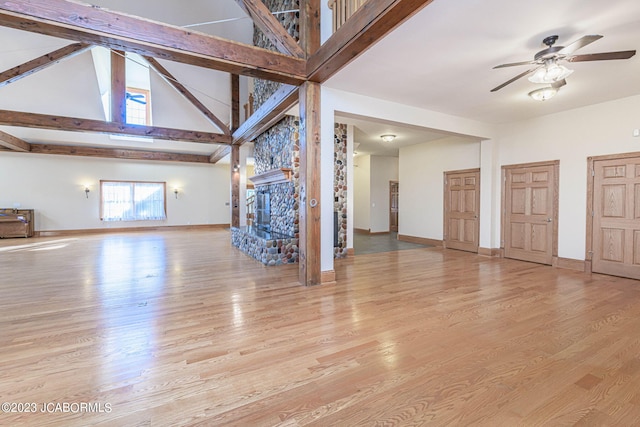 unfurnished living room featuring high vaulted ceiling, a stone fireplace, light hardwood / wood-style flooring, ceiling fan, and beamed ceiling