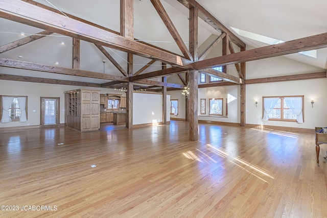 unfurnished living room featuring light hardwood / wood-style floors, beam ceiling, and high vaulted ceiling