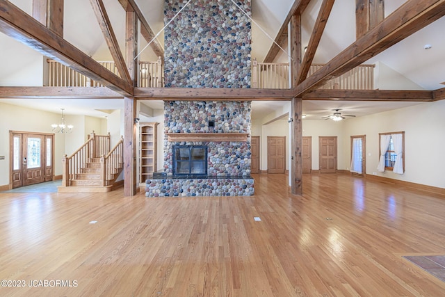 unfurnished living room with a stone fireplace, high vaulted ceiling, wood-type flooring, and ceiling fan with notable chandelier