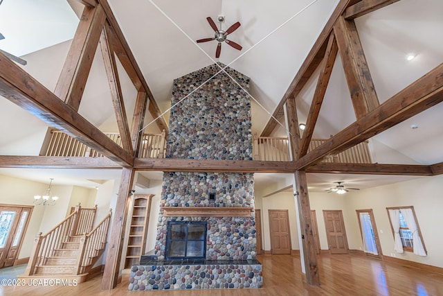 living room with a large fireplace, high vaulted ceiling, ceiling fan with notable chandelier, and light hardwood / wood-style flooring