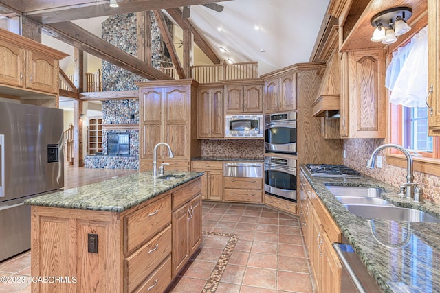 kitchen with stone counters, stainless steel appliances, a kitchen island with sink, and sink