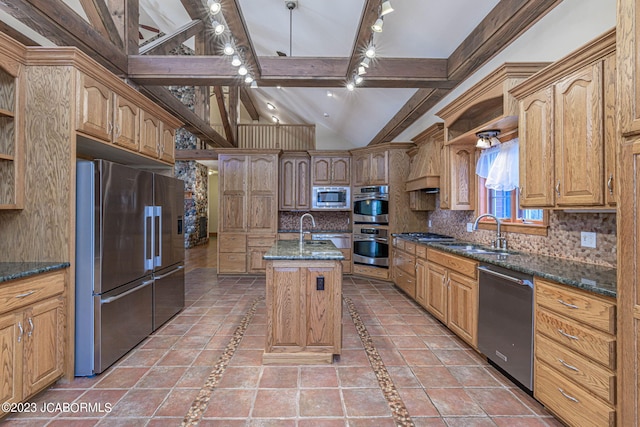 kitchen featuring sink, backsplash, dark stone countertops, a center island with sink, and appliances with stainless steel finishes