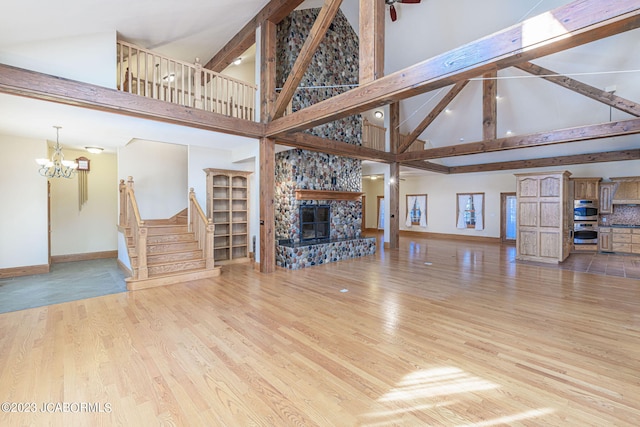 unfurnished living room featuring a stone fireplace, high vaulted ceiling, light hardwood / wood-style floors, and a notable chandelier