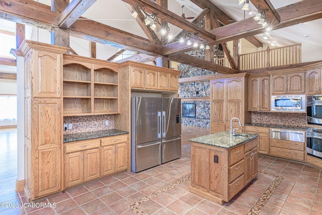 kitchen with dark stone countertops, an island with sink, tasteful backsplash, beamed ceiling, and stainless steel appliances