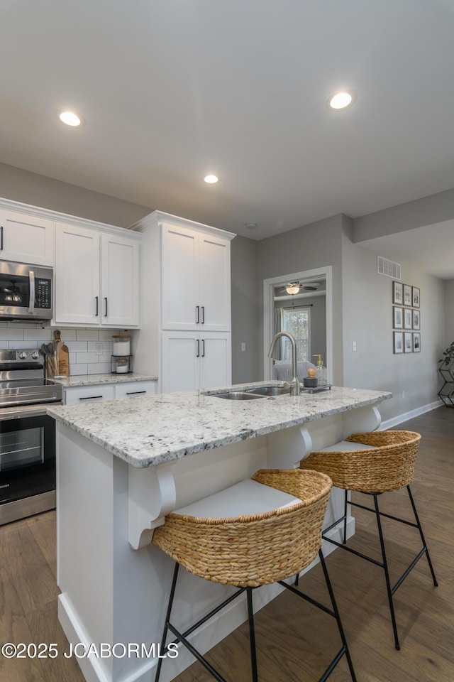 kitchen featuring visible vents, appliances with stainless steel finishes, a kitchen breakfast bar, and dark wood finished floors